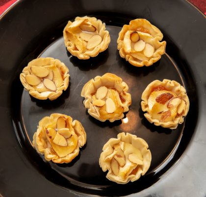 A black plate with mini fillo cups filled with warm sweet and creamy brie and apricots.