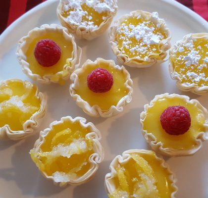 Fillo cups filled with lemon curd, dusted with confectioners sugar, and garnished with lemon zest.